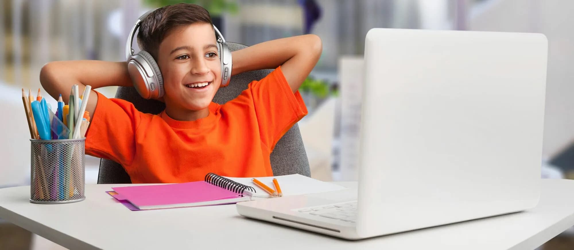 middle school boy sitting at his desk attending classes online, he wears headphones and is watching content on his laptop