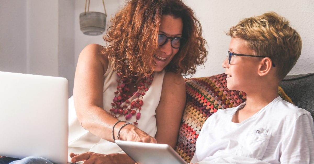 Adult and child with glasses using a laptop and tablet.
