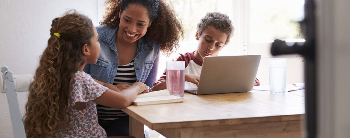 Adult and two children studying at a table with a book and laptop.