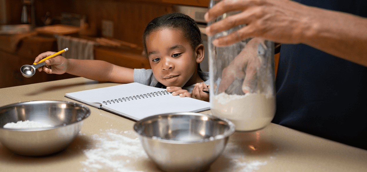 Child and adult baking, with flour, bowls, and a notebook on the counter.
