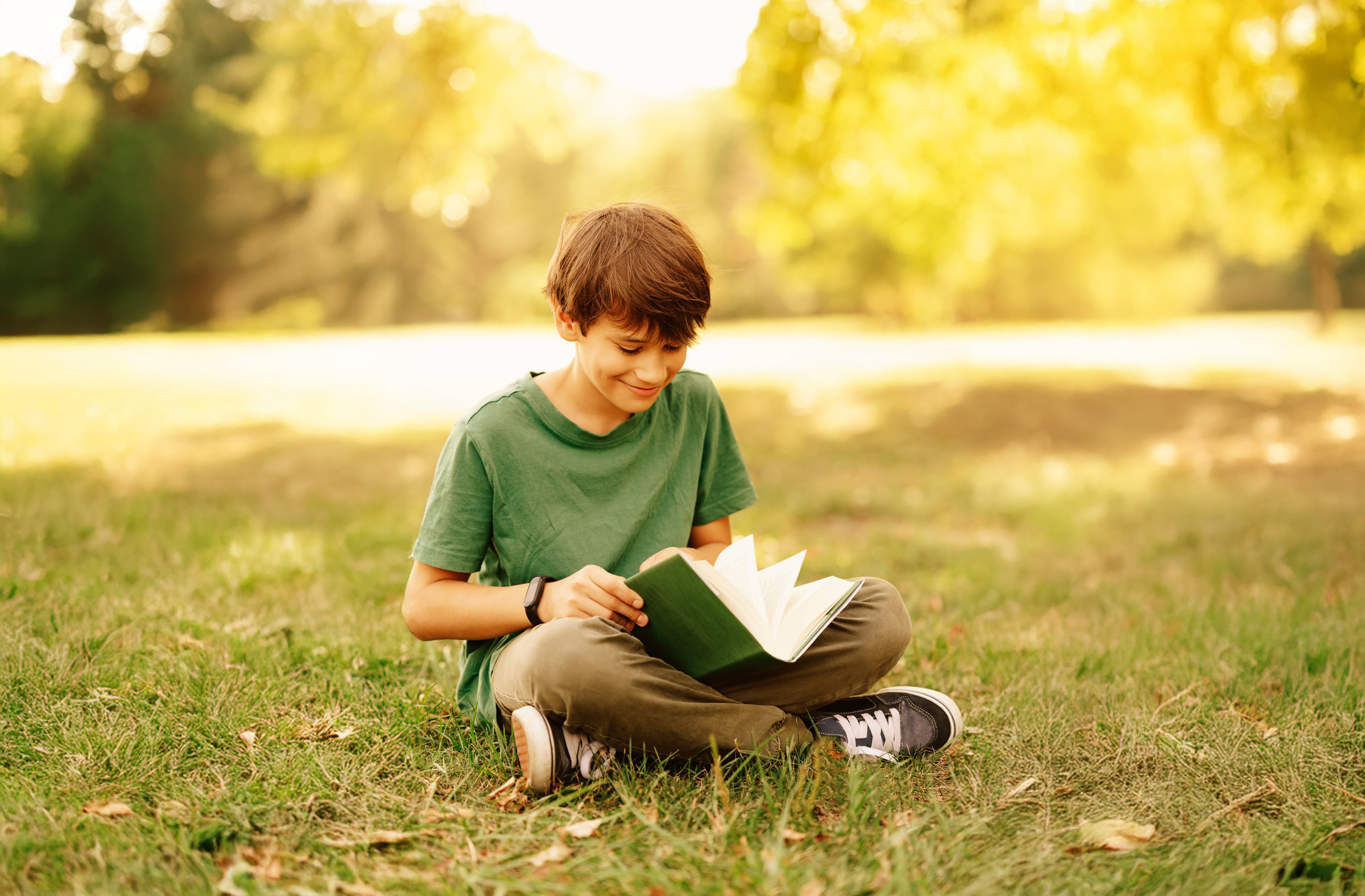 Child sitting on grass, smiling and reading a book.