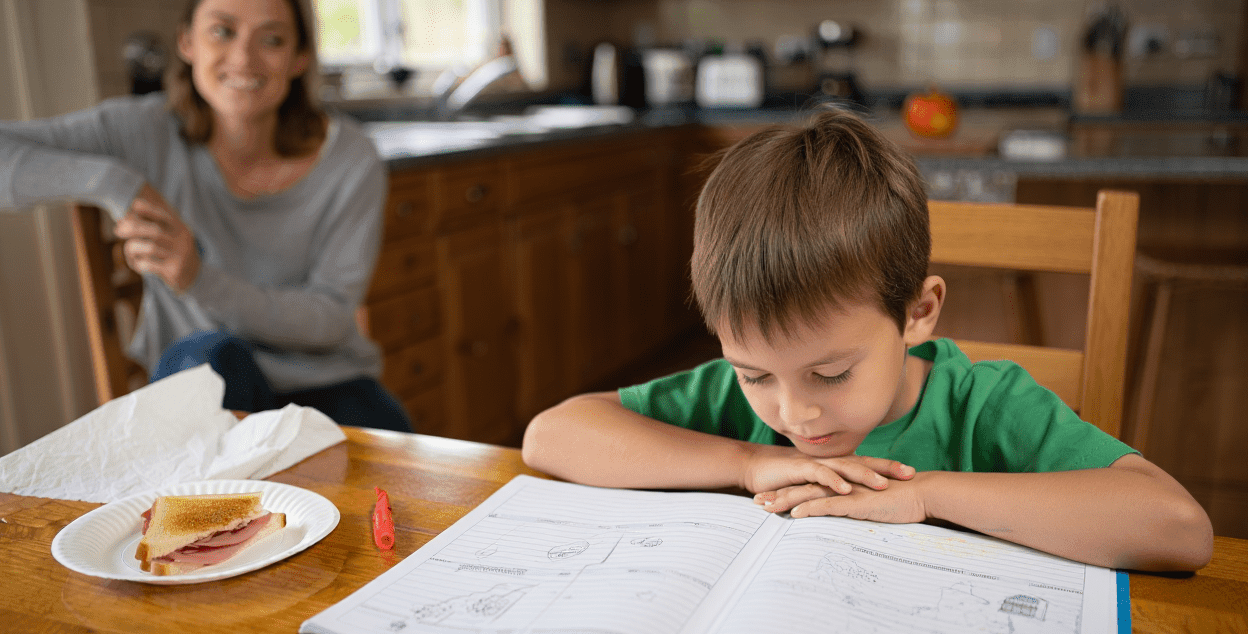 Child studying at a table with an adult nearby.