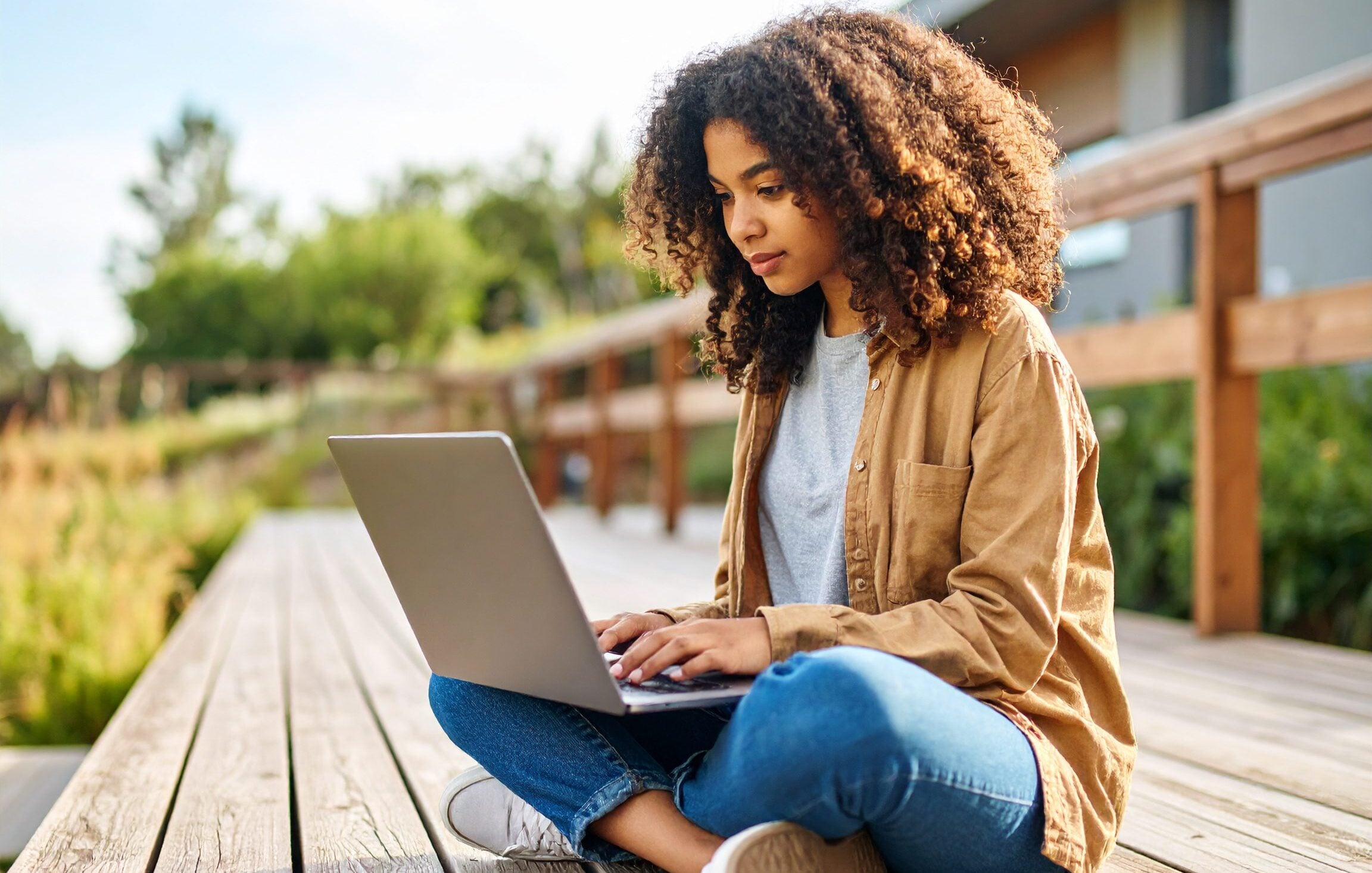 Young person with curly hair typing on a laptop outdoors.
