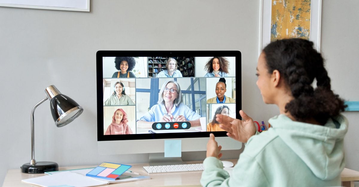 Student gestures at computer screen showing a video conference with seven adults.